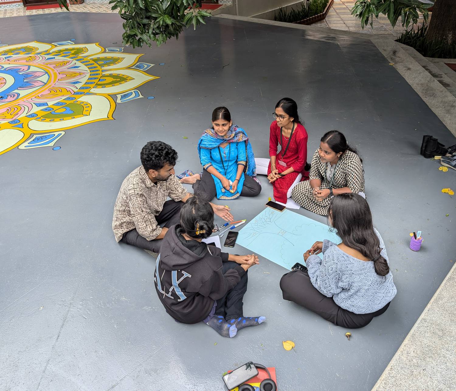 Young people sketching ideas on the floor beside a large painted rangoli