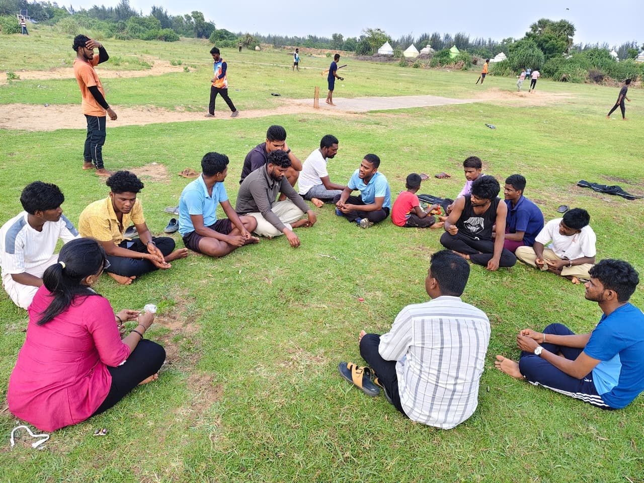 Young people sitting in a circle on a field near the coast